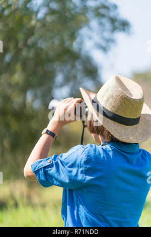 Donna usura hat e tenere premuto binocolo nel campo di erba Foto Stock