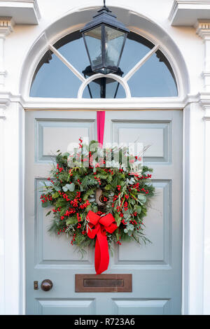 Corona di Natale con un nastro rosso sulla porta di una casa a Broadway. Cotswolds, Worcestershire, Inghilterra Foto Stock