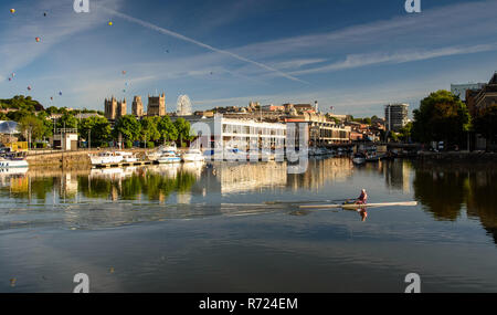 Bristol, Inghilterra, Regno Unito - 11 agosto 2018: un vogatore treni in Bristol flottante della banchine del porto su una mattina d'estate, mentre aria calda ballons galleggiare sopra il c Foto Stock