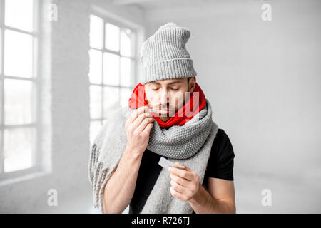 Ritratto di un uomo avvolto in un caldo foulard e sciarpe hat sensazione di cattivo misurare la temperatura corporea in ambienti chiusi. In inverno il concetto di malattia Foto Stock