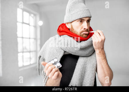 Ritratto di un uomo avvolto in un caldo foulard e sciarpe hat sensazione di cattivo misurare la temperatura corporea in ambienti chiusi. In inverno il concetto di malattia Foto Stock