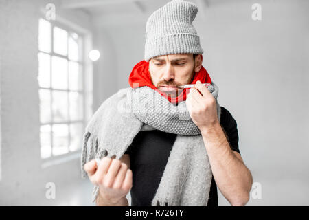 Ritratto di un uomo avvolto in un caldo foulard e sciarpe hat sensazione di cattivo misurare la temperatura corporea in ambienti chiusi. In inverno il concetto di malattia Foto Stock