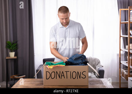 Giovane uomo donando vestiti in donazione Box sulla scrivania in legno Foto Stock