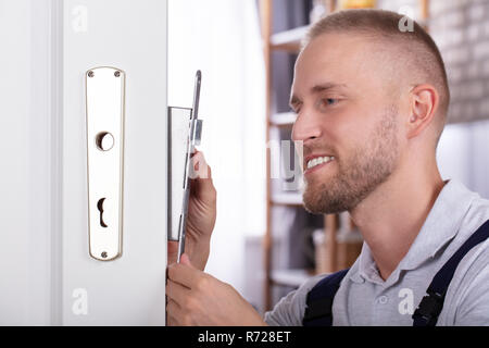 Close-up di un sorridente giovane uomo che fissa la serratura della porta in casa Foto Stock