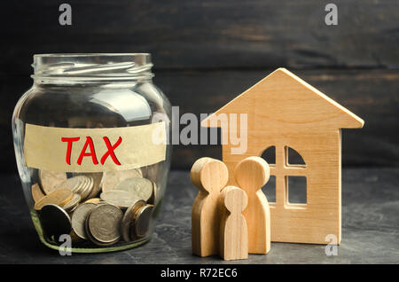 Vaso di vetro con le monete e la scritta "tassa" e una piccola casa. Le imposte sul patrimonio immobiliare, il pagamento. Penalità di mora. Registro dei contribuenti per proprietà. Foto Stock
