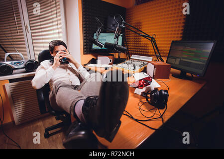 Ritratto di bel giovane uomo latino seduto davanti a un microfono con computer portatile presso la stazione radio Foto Stock