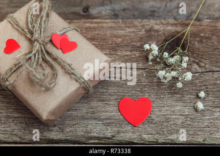 Confezione regalo presente avvolta carta craft con cuori rossi su rustiche vecchio alla moda vintage sfondo di legno. Natale felice vacanza biglietto di auguri anniversario Foto Stock