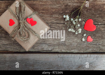 Confezione regalo presente avvolta carta craft con cuori rossi su rustiche vecchio alla moda vintage sfondo di legno. Natale felice vacanza biglietto di auguri anniversario Foto Stock