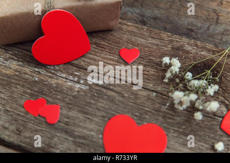 Confezione regalo presente avvolta carta craft con cuori rossi su rustiche vecchio alla moda vintage sfondo di legno. Natale felice vacanza biglietto di auguri anniversario Foto Stock