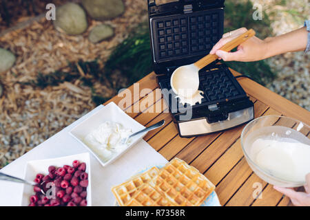 Preparazione di waffles fatti in casa. Versare l'impasto in waffle ferri da stiro con un mestolo all'aperto in giardino Foto Stock