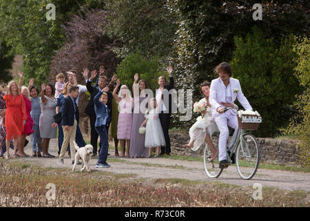 Gli ospiti dei matrimoni sventolando off sposi novelli su biciclette Foto Stock