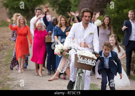 Gli ospiti dei matrimoni sventolando off sposi novelli su biciclette Foto Stock