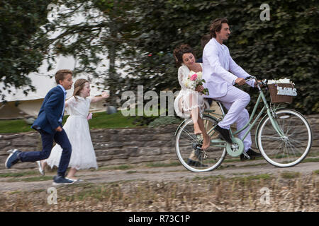 I giovani ospiti di nozze in esecuzione dopo sposi novelli su biciclette Foto Stock