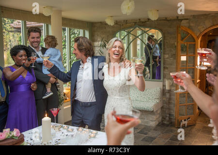 Gli ospiti dei matrimoni tostare per novelli sposi presso la reception Foto Stock