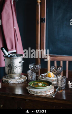 Ciotola di fresco guarnita di zuppa, un dessert e champagne sulla tavola vintage Foto Stock