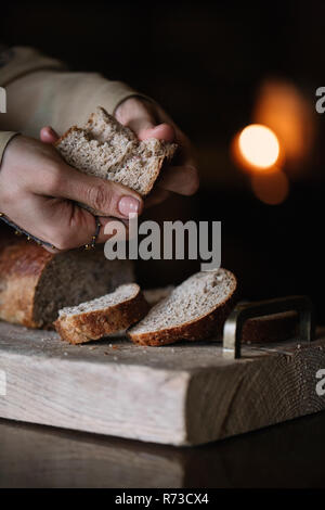 Giovane donna spezzare il pane marrone rustico tagliere, close up delle mani Foto Stock