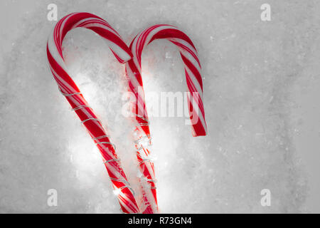 Natale candy canes illuminato da garland e collocato sul bianco della neve Foto Stock