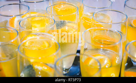 Bicchieri di champagne su un vassoio con prosecco e fettine di arancia sotto la luce diretta del sole