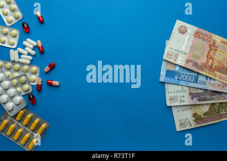 Pillole con rubli denaro isolato su sfondo blu. Spese di medicina. Costi elevati del concetto di medicazione. Posto per il testo Foto Stock