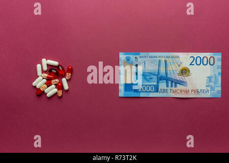 Pillole con rubli denaro isolato su sfondo di borgogna. Spese di medicina. Costi elevati del concetto di medicazione. Foto Stock