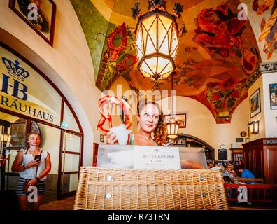 Monaco di Baviera, Germania - 29 Luglio 2018: giovane attraente cameriera vende giganti pretzel alla mitica Hofbrauhaus sala della birra di Monaco di Baviera, Germania - ultra wide Foto Stock