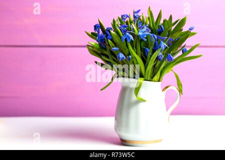 Snowdrops in un vaso su una tabella su un sfondo rosa Foto Stock