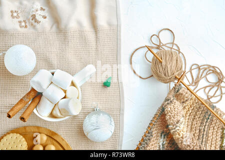 Cioccolata calda con biscotti, marshmallows, decorazioni di Natale, miniatura albero di Natale e sciarpa maglia strumenti sul tavolo Foto Stock
