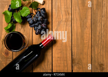 Bottiglia e bicchiere di vino grappoli di uva e foglie di vite su sfondo di legno. Vista da sopra con copia spazio. Foto Stock