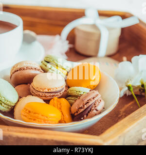 Dolce colazione a letto per amante. Close up amaretti, tazza di caffè, fiore e confezione regalo sul vassoio in legno Colazione romantica a letto. Compleanno, Valentin Foto Stock