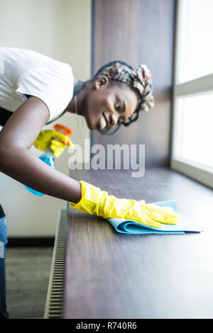 Ritratto di giovane afro american donna in giallo guanti davanzale di lavaggio con un panno e il detergente per vetri per interni Foto Stock