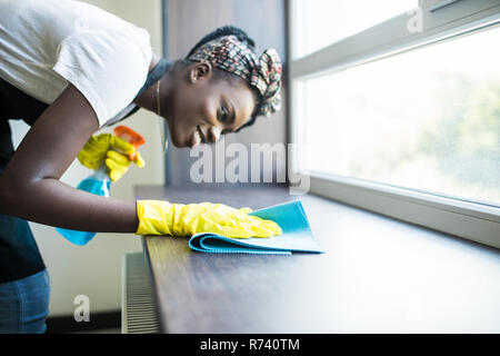 Ritratto di giovane afro american donna in giallo guanti davanzale di lavaggio con un panno e il detergente per vetri per interni Foto Stock