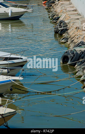 Diverse barche ormeggiate sulla riva con rocce nel marina con pneumatici di protezione Foto Stock