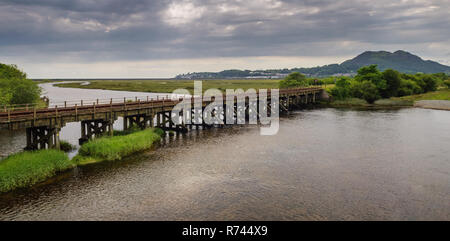 Il Cambrian Coast Line attraversa il fiume Glaslyn e i campi e le saline di Traeth Mawr a Portmadog nel Galles del Nord. Foto Stock