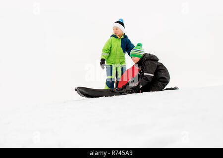 I bambini lo scorrimento su slittini giù collina di neve in inverno Foto Stock