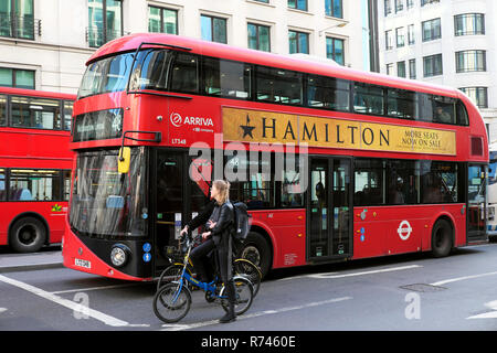 Red double-decker bus con inserzione sul lato americano per la West End theatre play Hamilton e i ciclisti in attesa su biciclette a Londra REGNO UNITO KATHY DEWITT Foto Stock