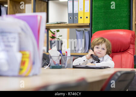 Little Boy siede in ufficio in cattedra e parlando al telefono. Piccolo boss. Foto Stock