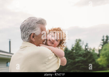 Toddler femmina con ricci capelli rossi in nonno di braccia, ritratto Foto Stock