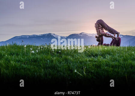 Due giovani donne praticanti acroyoga sul prato di fronte all mountain range al tramonto, Squamish, British Columbia, Canada Foto Stock