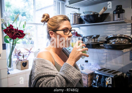 Gravidanza metà donna adulta di bere succo di frutta fresco in cucina Foto Stock