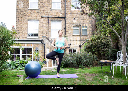 Gravidanza metà donna adulta a praticare yoga la posizione dell'albero nel giardino Foto Stock