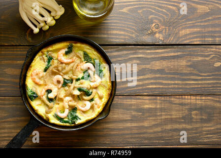 La frittata, funghi e spinaci frittata con gamberetti in padella su sfondo di legno con copia spazio. Vista superiore, laici piatta Foto Stock