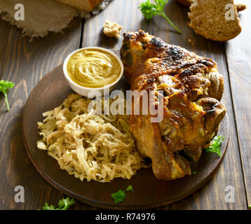 Carne di maiale al forno il fuso a snodo (eisbein) con brasato di cavolo (crauti) e senape su un tavolo di legno. Foto Stock