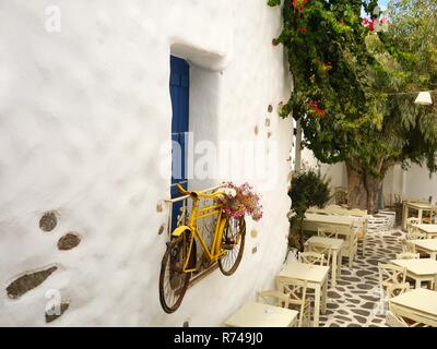 Bicicletta decorative appese su una finestra in corrispondenza di un ristorante esterno con tavoli e un bellissimo albero in fiore Foto Stock