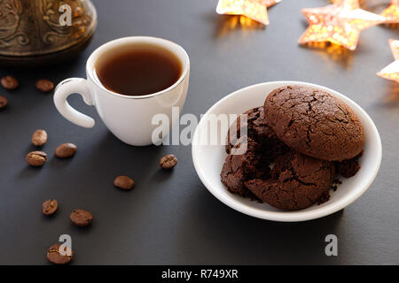 Sbriciolato biscotti al cioccolato e caffè in tazza piccola su uno sfondo scuro e le luci di Natale Foto Stock