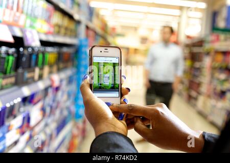 Carrello utilizzando un telefono intelligente per eseguire la scansione dei codici a barre dei beni di consumo in un supermercato Foto Stock