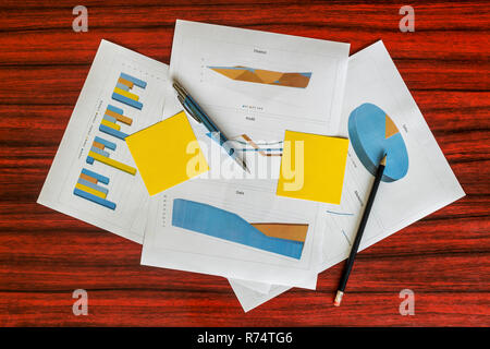 Mazzetto di stampare grafici e diagrammi con note di giallo, fermagli per carta e penna su di essi Foto Stock