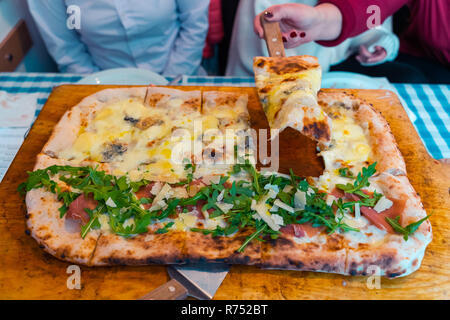 Pizza Napoletana sul tavolo del ristorante. Italian pizza fresca sul piatto di legno. Mano Womans prendendo una fetta. Quattro Formaggi, margarita. Foto Stock