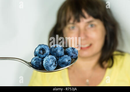 Fresco di mirtilli succosa con gocce d'acqua sul cucchiaio in acciaio inox. Vaccinium myrtillus. Blu mirtilli neri di close-up. Donna su sfondo. Medicina alternativa. Foto Stock