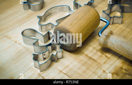 Utensili da cucina per la preparazione di Xmas gingerbreads. Ancora in vita con un piccolo perno di rotolamento per l'impasto. Tagliatori di metallo di varie forme su legno spianatoia. Foto Stock