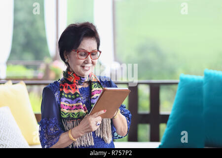 Asian senior donna seduta sul divano e utilizzando un tablet Foto Stock
